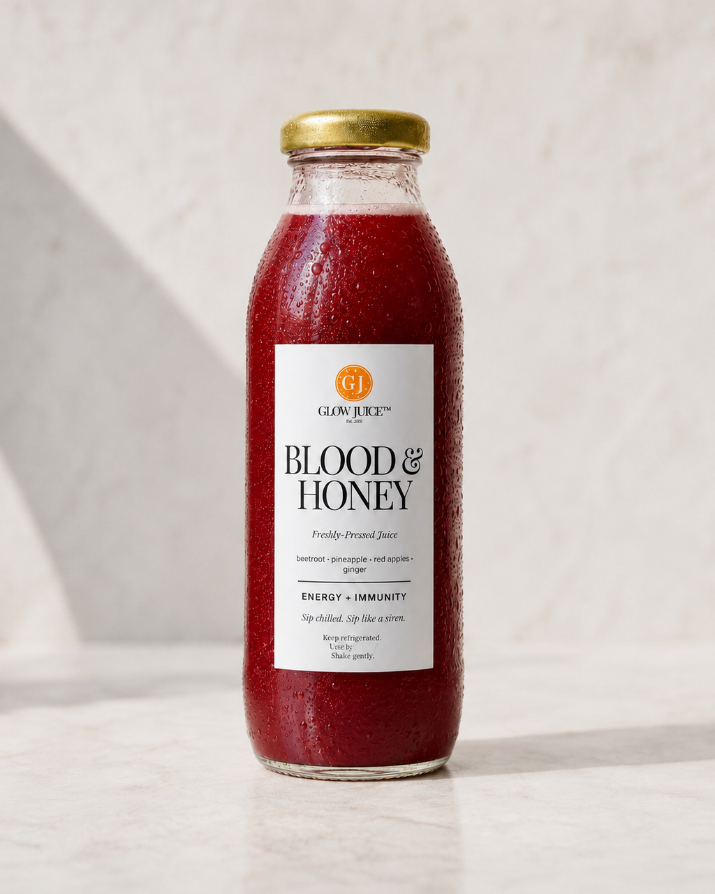A glass bottle of Glow Juice Blood & Honey drink with a gold cap, filled with a deep red beverage, set against a light marble background.