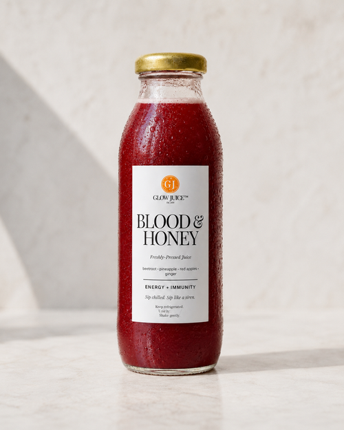 A glass bottle of Glow Juice Blood & Honey drink with a gold cap, filled with a deep red beverage, set against a light marble background.