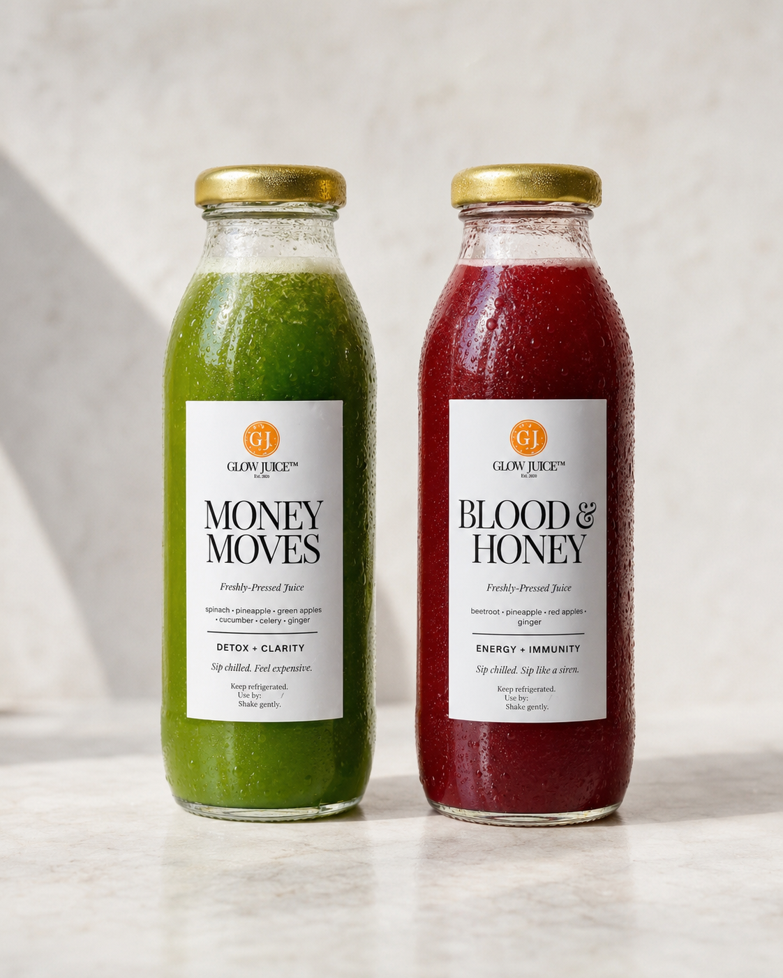 Two glass bottles of Glow Juice juices on a light marble surface against a textured light grey wall. The left bottle contains a green juice labelled 'Money Moves' and the right bottle contains a dark red juice labelled 'Blood & Honey'.